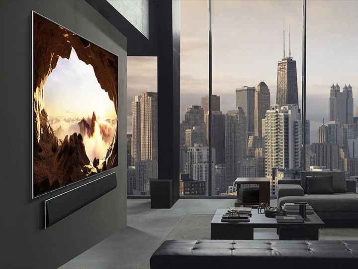 Просторная гостиная с видом на городской пейзаж. Телевизор LG OLED TV установлен на стене со звуковой панелью LG Soundbar. Вид сбоку на телевизор с дизайном One Wall Design и ультратонкой рамкой, что позволяет ему хорошо вписываться в интерьер. Приставку для нулевого подключения видно, хоть она и скрыта. 